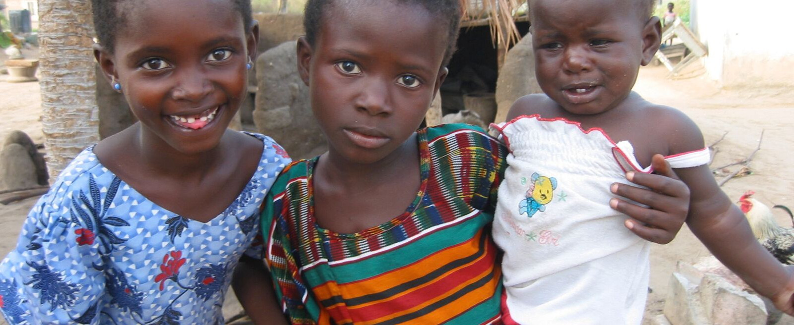 Three children together outdoors, one holding a younger child
