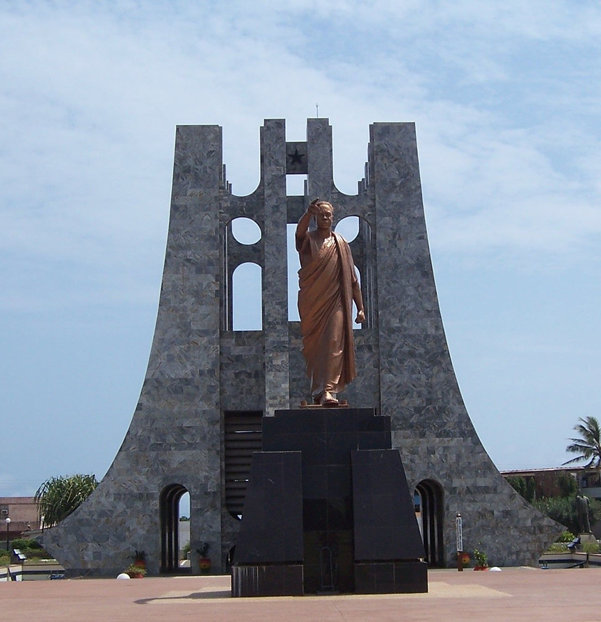 A statue standing before a tall stone monument
